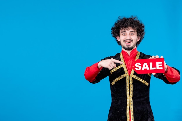 Free photo portrait of happy azeri man in traditional costume holding sale nameplate blue background shopping novruz ethnic concept spring