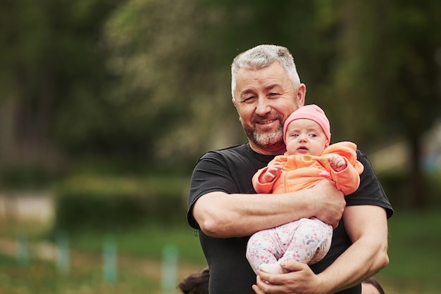 Portrait of happy bearded grandfather holding child in the park
