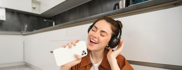 Free photo portrait of happy beautiful girl sings songs in headphones listens to music using smartphone as mic