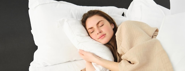 Free photo portrait of happy beautiful young woman resting in bed wearing pyjamas hugging her pillow and