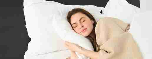 Free photo portrait of happy beautiful young woman resting in bed wearing pyjamas hugging her pillow and