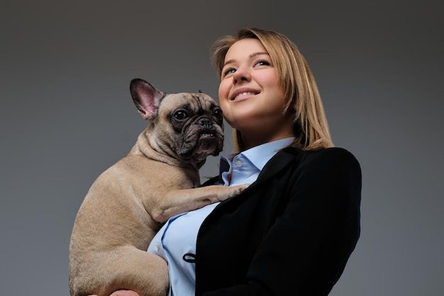 Portrait of a happy blonde woman breeder holds her cute pug. Isolated on a gray background.