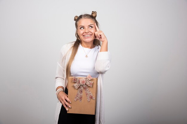 Portrait of happy blonde woman with gift box thinking.