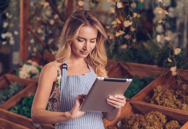 Ritratto di un giovane fiorista bionda bionda felice utilizzando la tavoletta digitale