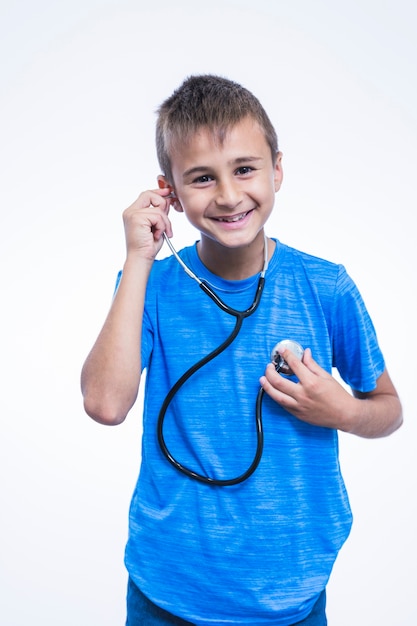 Foto gratuita ritratto di un ragazzo felice ascoltando il suo battito cardiaco con stetoscopio