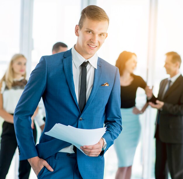 Portrait of a happy businessman holding documents with colleagues in background