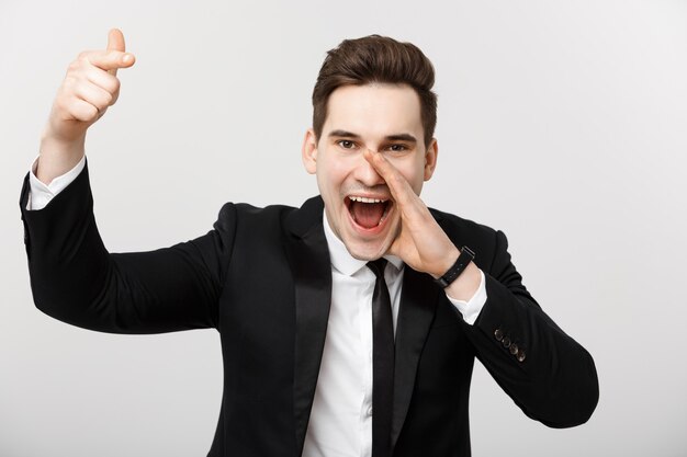 Portrait of a happy businessman in suit pointing finger away over isolated grey background