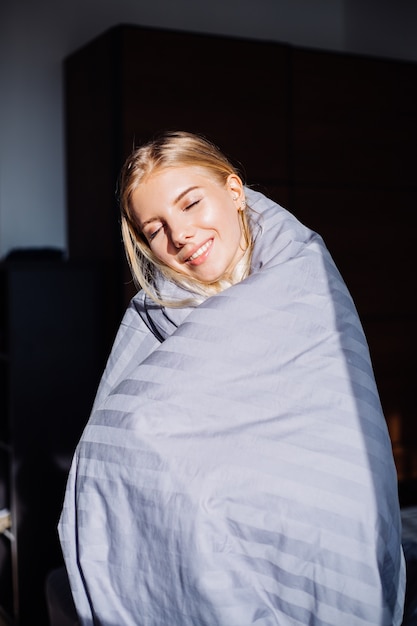 Portrait of happy calm woman in bedroom in gray stripped blanket and black and beige body, home sleep wear