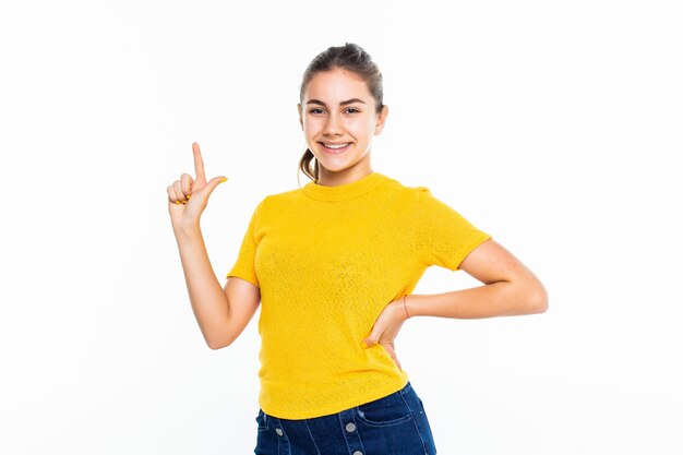 Portrait of a happy casual girl pointed up against white wall