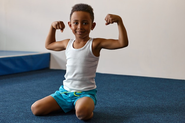 Free photo portrait of happy cheerful dark skinned boy with short afro hairstyle exercising at fitness center