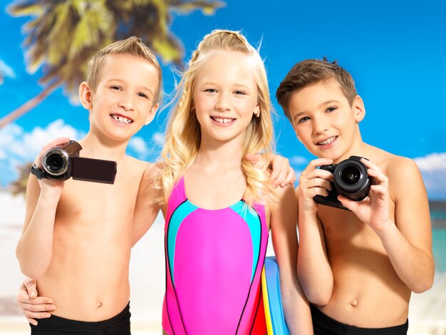 해변에서 즐기는 행복 한 어린이의 초상화입니다. 손에 사진 및 비디오 카메라와 함께 서있는 학생 아이.