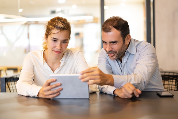 Portrait of happy colleagues browsing on digital tablet at cafe