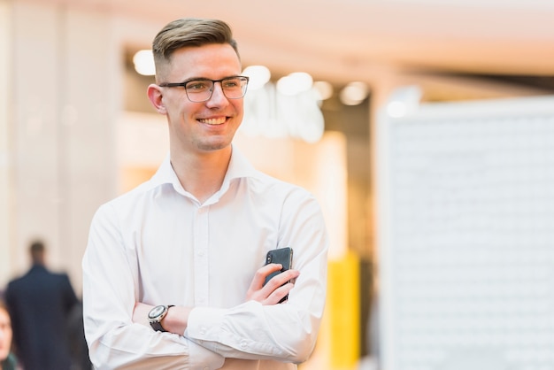 Foto gratuita il ritratto di giovane uomo d'affari sicuro felice con il braccio ha attraversato il telefono cellulare della tenuta a disposizione