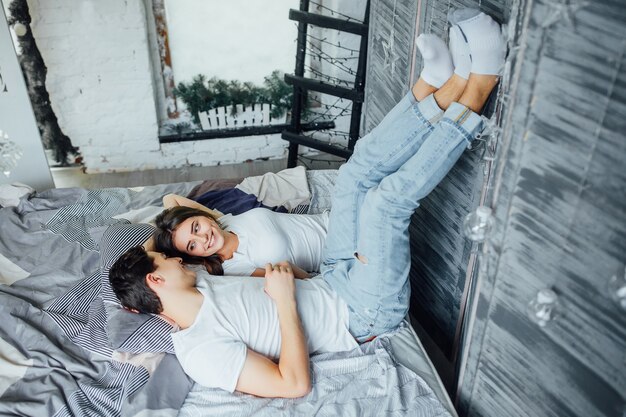 Portrait of happy couple relaxing in bed and holding hands and legs at morning