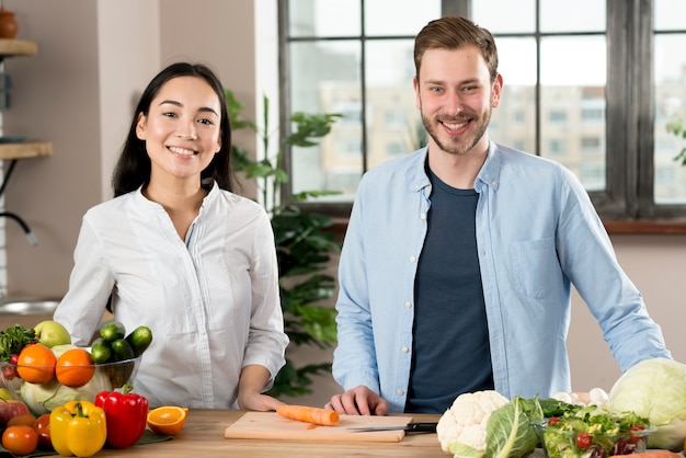 野菜の種類とキッチンカウンターの後ろに立っている幸せなカップルの肖像画