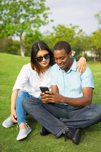 Portrait of happy couple watching photos on smartphone in park.