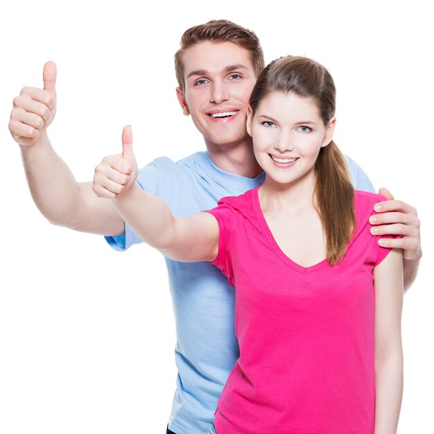 Portrait of happy couple with thumbs up sign isolated on white wall.