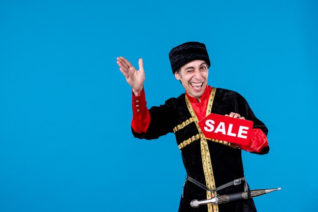 Portrait of happy curious young adult in traditional dress and showing sale icon on blue wave background