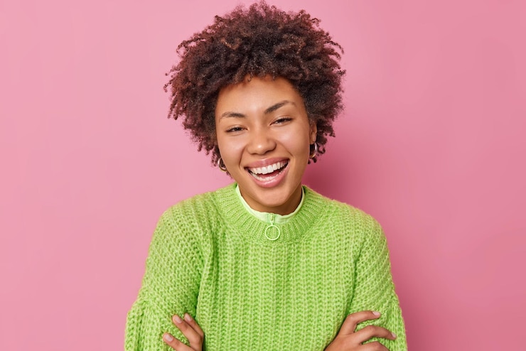 Free Photo portrait of happy curly haired young woman smiles positively wears casual green knitted sweater has upbeat mood expresses positive emotions poses against pink background hears pleasant news.