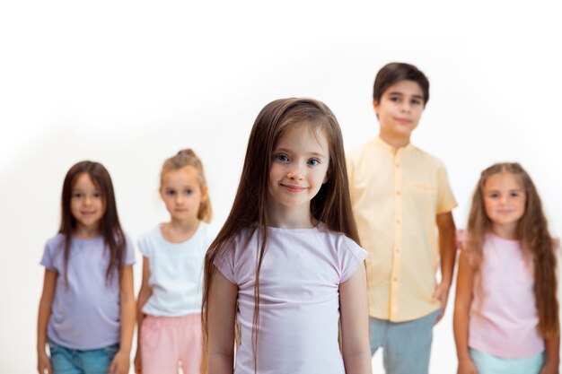 The portrait of happy cute little kids boy and girls in stylish casual clothes looking at camera against white wall