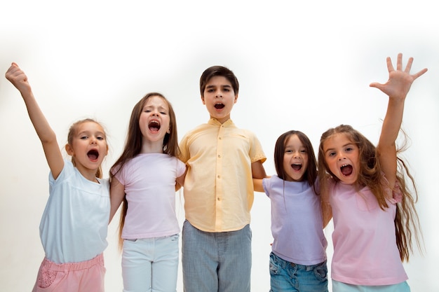 The portrait of happy cute little kids boy and girls in stylish casual clothes looking at front against white studio wall