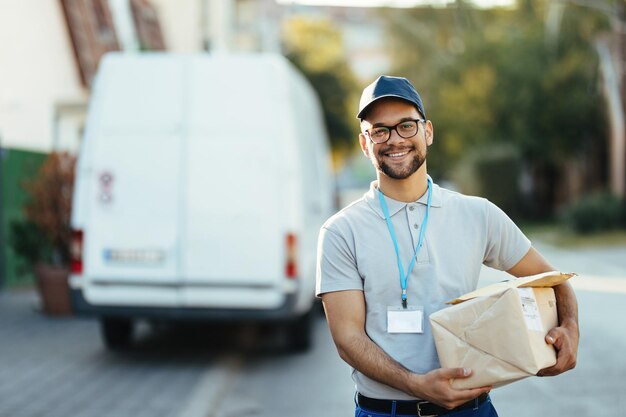 portrait of happy delivery man carrying packages and looking at camera while standing on the street