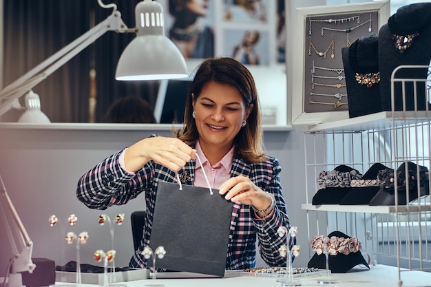 Portrait of happy elegantly dressed woman seller packs precious earrings in a box for her client in a luxury jewelry store.