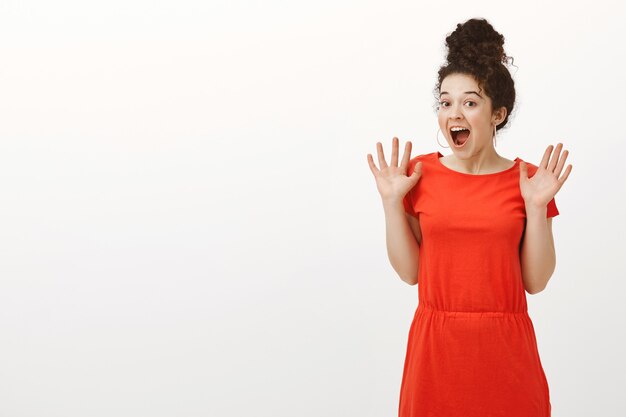 Portrait of happy excited caucasian curly-haired woman with bun haircut, smiling broadly and screaming from amazement and surprise