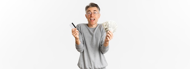 Free photo portrait of happy and excited middleaged man showing credit card and money standing amazed over whit