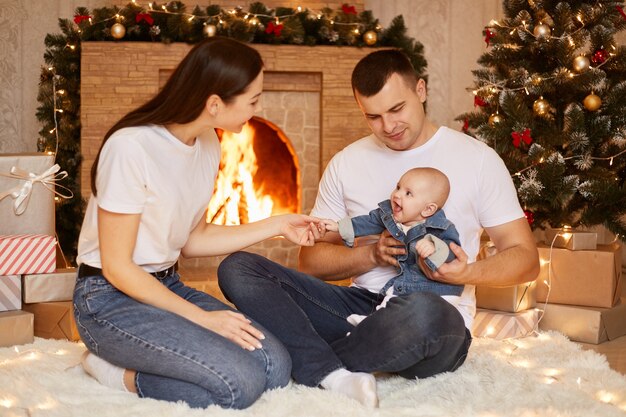 幸せな家族、父、母、幼児の娘が自宅の暖炉とクリスマスツリーでポーズをとり、冬の休暇を一緒に祝うことを幸せに、幸せな新年を迎える肖像画。