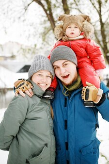 Portrait of happy family with one kid in winter casual outfit posing outdoors in snow public park