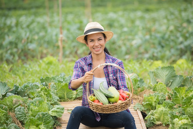 Portrait of happy female farmer holding a basket of vegetables in the farm