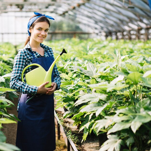 Portrait of a happy female gardener holding watering can in greenhouse