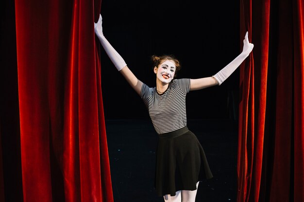 Portrait of a happy female mime artist holding red curtain