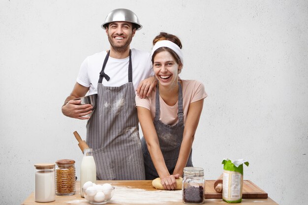 Portrait of happy female model kneads dough with smile, stands near male colleague, work together