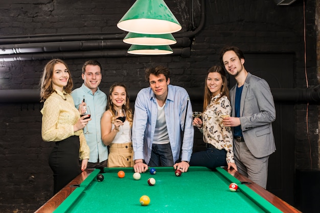 Free photo portrait of happy friends standing behind snooker table enjoying in club