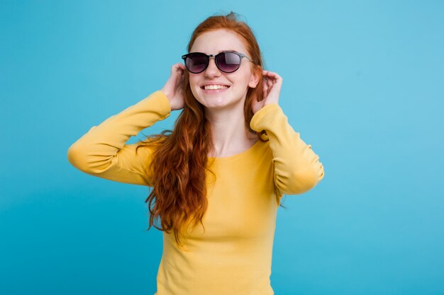 Portrait of happy ginger red hair girl with freckles smiling looking at camera. Pastel blue background. Copy Space.