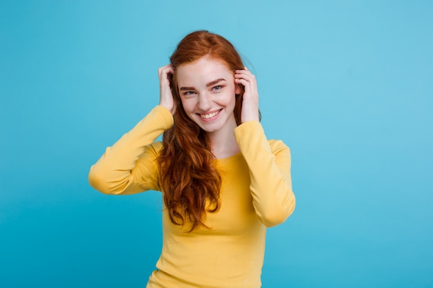 Portrait of happy ginger red hair girl with freckles smiling looking at camera. Pastel blue background. Copy Space.