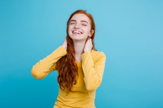 Portrait of happy ginger red hair girl with freckles smiling looking at camera. Pastel blue background. Copy Space.