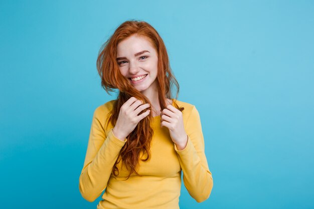 Portrait of happy ginger red hair girl with freckles smiling looking at camera. Pastel blue background. Copy Space.