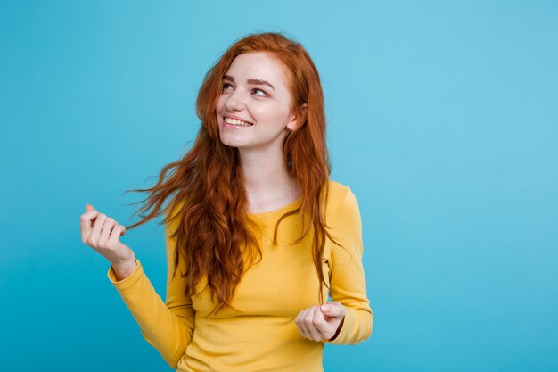 Portrait of happy ginger red hair girl with freckles smiling looking at camera. Pastel blue background. Copy Space.