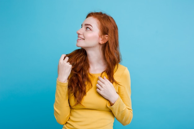 Portrait of happy ginger red hair girl with freckles smiling looking at camera. Pastel blue background. Copy Space.