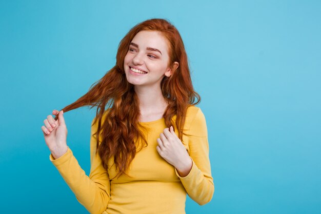 Portrait of happy ginger red hair girl with freckles smiling looking at camera. Pastel blue background. Copy Space.