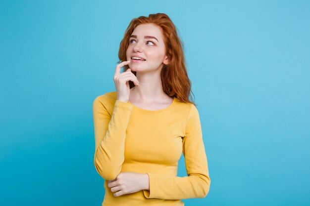 Portrait of happy ginger red hair girl with freckles smiling looking at camera. Pastel blue background. Copy Space.