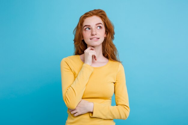 Portrait of happy ginger red hair girl with freckles smiling looking at camera. Pastel blue background. Copy Space.