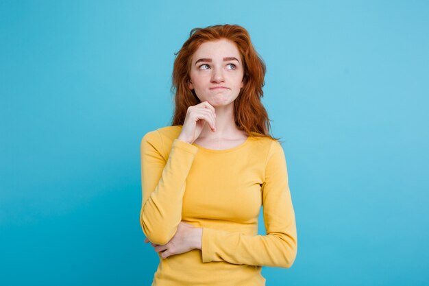 Portrait of happy ginger red hair girl with freckles smiling looking at camera. Pastel blue background. Copy Space.