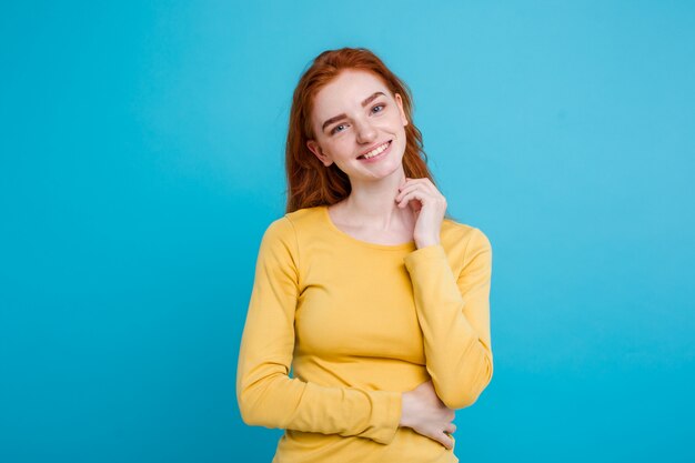 Portrait of happy ginger red hair girl with freckles smiling looking at camera. Pastel blue background. Copy Space.