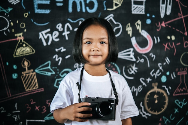 디지털 카메라를 들고 있는 행복한 소녀의 초상화, 어린 사진작가 소녀는 카메라를 사용하여 사진을 찍는 것을 즐깁니다.