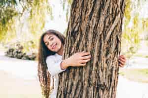 Foto gratuita ritratto di una ragazza felice che abbraccia il grande tronco nel giardino