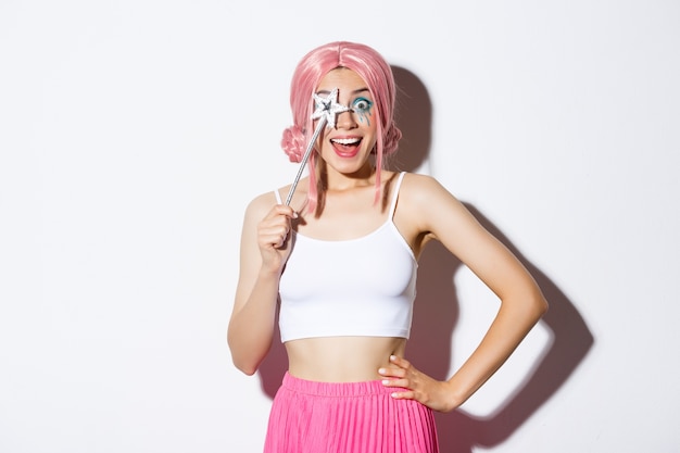 Free photo portrait of happy girl smiling, celebrating halloween in fairy costume, with pink wig and bright makeup, holding magic wand, looking excited.